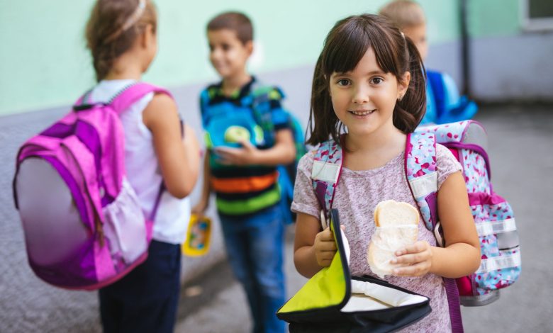 niña feliz entrando a la escuela con su lonchera